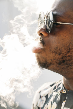 Black stylish man wearing sunglasses. He is vaping with an electronic cigarrete outdoor
