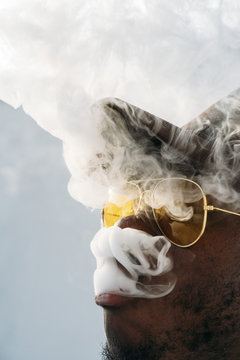 Black stylish man wearing sunglasses. He is vaping with an electronic cigarrete outdoor