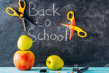 apple, scissors and school supplies against blackboard with "back to school" on background