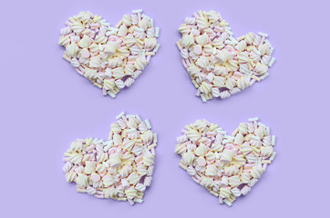 Colorful marshmallow laid out on violet and pink paper background. pastel creative textured hearts....