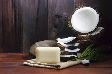 Coconut soap with coconut half and coconut pieces and leaf on wooden table.