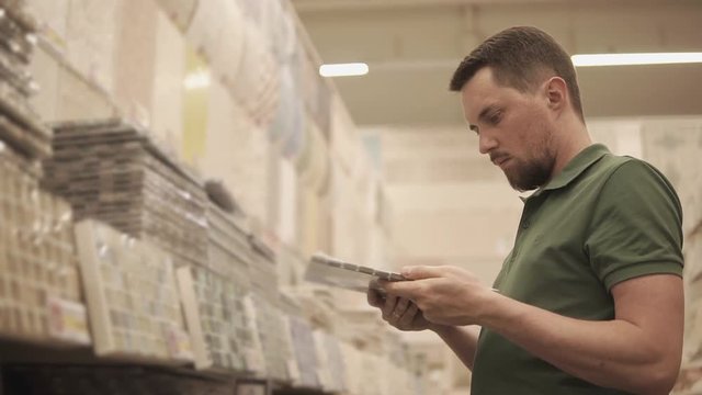young man is considering a tile, maybe he will use it for floor covering or else he will put it on the walls in the bathroom, the gentleman was going to do repairs and came to the construction market