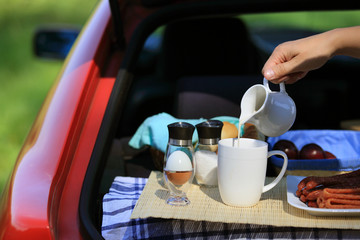 Kobieca ręka nalewa mleko do kubka, piknik w bagażniku samochodu. - obrazy, fototapety, plakaty