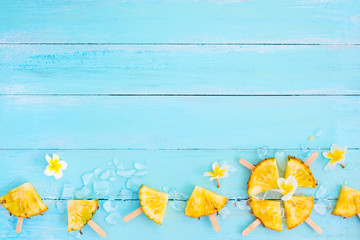 Pineapple popsicle sticks with ice on wood plank blue color. summer fruit concept, top view