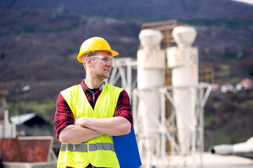 Male engineer wearing reflective vest and hardhat standing with clipboard