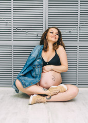 Stylish beautiful pregnant woman sitting on the floor and posing on camera. Pregnancy concept.