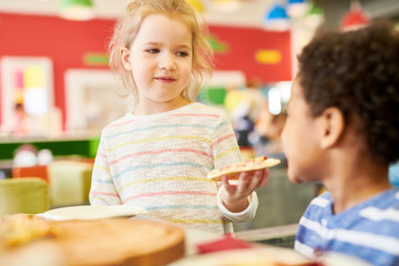 Colorful portrait of children eating pizza enjoying awesome  party in cafe, focus on cute blond girl offering pizza to friend