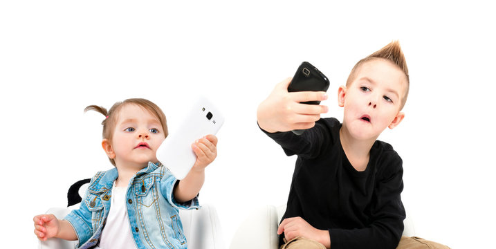 Portrait of attractive cheerful boy and cute little girl taking selfie on mobile phone, isolated on a white background