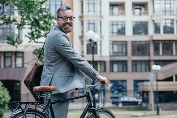 bearded handsome businessman standing with bike on street in city