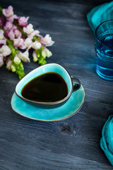 Black coffee in a turquoise cup and flowers on a black background. Low key, free space