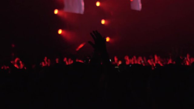 Slow motion shot of unidentified singer performing in front of crowded music hall. People dancing with hands up and taking mobile videos