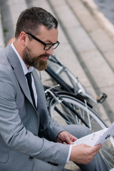 Fototapeta na wymiar handsome bearded businessman reading newspaper on stairs with bicycle