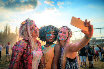Multiethnic girls covered in colorful powder taking selfie at summer holi festival