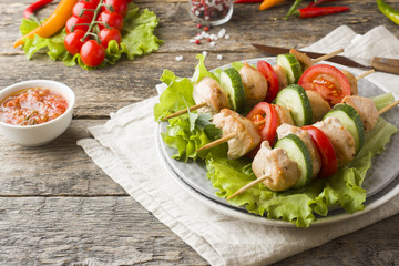 Traditional chicken kebab on wooden skewers with tomatoes, cucumbers and fresh herbs on a plate.