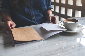 Closeup image of a woman opening a book with coffee cup on table in modern cafe