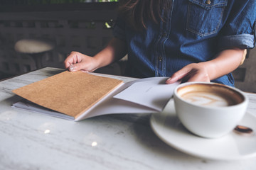 Closeup image of a woman opening a book with coffee cup on table in modern cafe