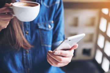 Closeup image of a woman holding , using and touching a smart phone while drinking coffee