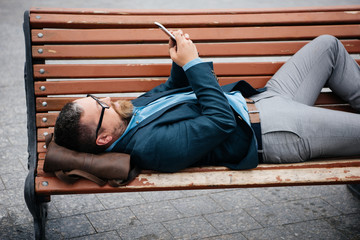 businessman using smartphone lying on bench in city