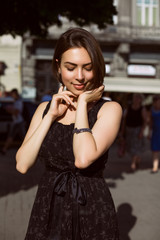 Smiling brunette girl with bronze tan posing on the street in a fashionable dress