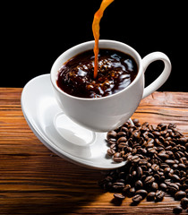 Coffee is poured into cup on wooden background with coffee beans.