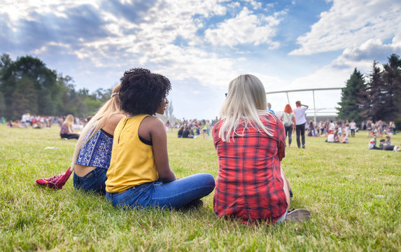 Group of friends at summer music festival sitting on grass