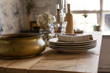 Closeup photo of a wooden table with porcelain plates, tissue napkin and copper container