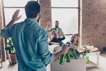 Rear view of visitor bringing bottles with beer to his stylish, successful, attractive friends  who...