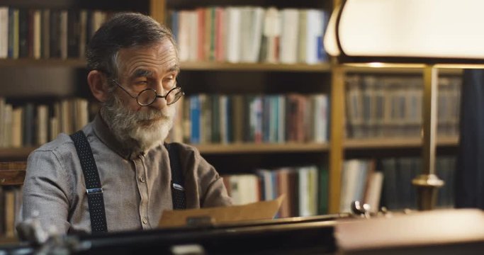 Old Caucasian man reading some ancient document or letter while working at the library and thinking about it.