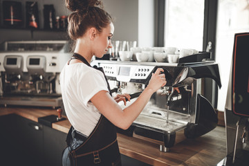 Young woman barista preparing coffee using machine in the cafe - obrazy, fototapety, plakaty