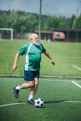 elderly bearded man playing football on field on summer day