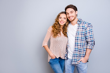 Portrait with copysapce empty place of attractive successful couple in casual outfits holding hands in pocket of pants hugging looking at camera isolated on grey background
