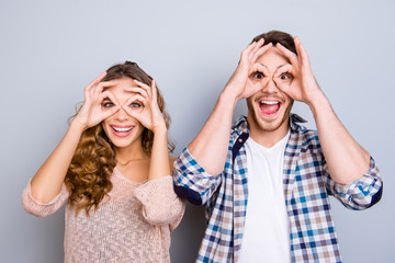 Portrait of childish cool couple making binoculars with fingers around eyes keeping mouth open...