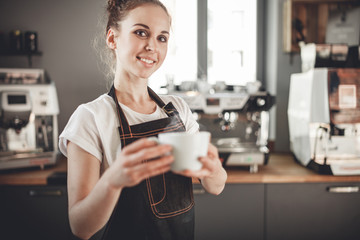 Smiling barista woman presents cup of hot coffee at cafe, coffee shop business