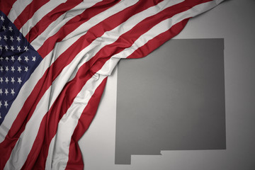 Naklejka premium waving national flag of united states of america on a gray new mexico state map background.