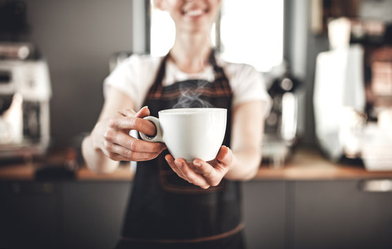 Smiling barista woman presents cup of hot coffee at cafe, coffee shop business