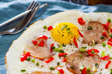 fried egg with ham sausage and pepper in a white plate on table
