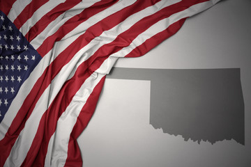 waving national flag of united states of america on a gray oklahoma state map background.