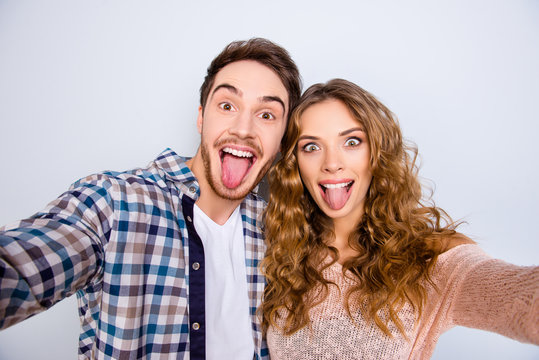 Self portrait of crazy funky couple gesturing tongue out having online meeting shooting selfie on front camera isolated on grey background