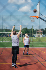 elderly men playing basketball together on playground on summer day