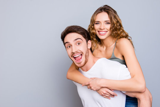 Portrait with copy space empty place of cheerful positive couple, amazed man carrying on back pretty toothy woman isolated on grey background. Advertisement concept