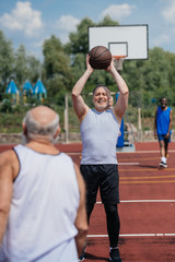 selective focus of old multiethnic friends playing basketball on summer day