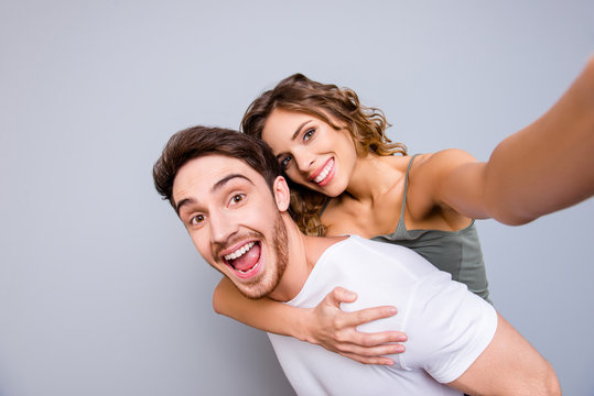 Rest relax leisure concept. Self portrait of positive cheerful couple, excited man carrying on back pretty lover shooting selfie on front camera isolated on grey background