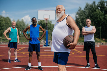 Fototapeta na wymiar selective focus of multiethnic elderly sportsmen with basketball ball on playground