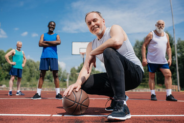 selective focus of multiethnic elderly sportsmen with basketball ball on playground