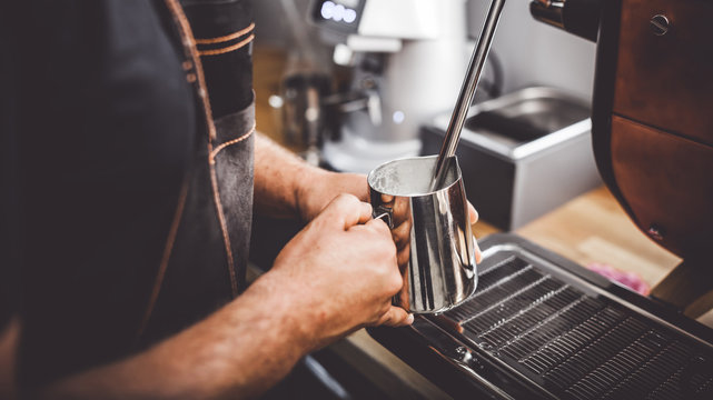Barista steaming milk using coffee machine, close up view on hands during preparation