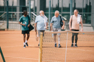 Fototapeta na wymiar selective focus of multiracial elderly friends with tennis equipment on court
