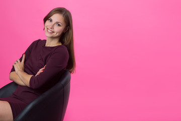 beautiful young girl with a smile on her face with flowing hair on a pink background sitting in a...