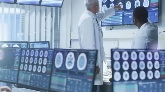Team of Professional Scientists Work in the Brain Research Laboratory. Neurologists / Neuroscientists Surrounded by Monitors Showing CT, MRI Scans Having Discussions. Shot on RED EPIC-W 8K.