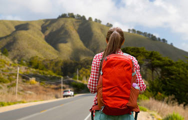 travel, tourism and hike concept - young woman with backpack over big sur of california hills background