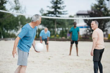 selective focus of multicultural old friends playing volleyball on beach on summer day